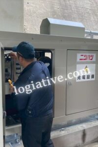 Male technician in a dark blue uniform servicing an outdoor electrical control panel in a gray metal cabinet.